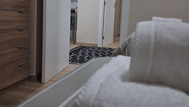 A bedroom with a bed, a wooden dresser, and a hallway leading to a kitchen. - Arco-Íris, Ponta do Sol (Ponta do Sol)