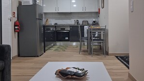 A modern kitchen with white cabinets, a grey refrigerator, and a dining area with a white table and chairs. - Arco-Íris, Ponta do Sol (Ponta do Sol)