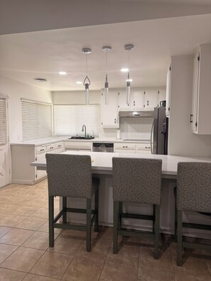 A modern kitchen with white cabinets, a central island with bar stools, pendant lighting, and a dishwasher.