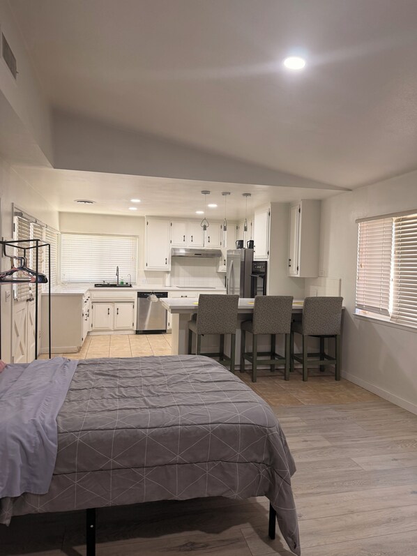 A compact room with a bed, a kitchenette, and a dining area with chairs.