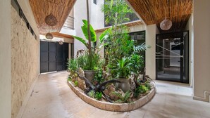 Un patio con una jardinera central, techo de bambú y una puerta con panel de vidrio.