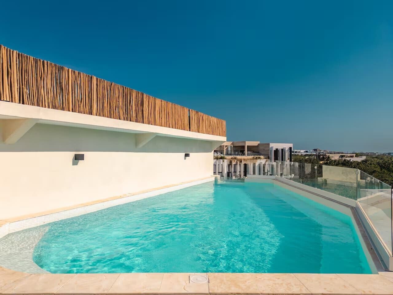 A rooftop pool with clear blue water, a wooden slatted wall, and a view of the cityscape.