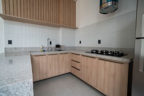 A modern kitchen with wooden cabinets, a granite countertop, and a built-in gas stove. - Moov Smart Home (Cuiabá)