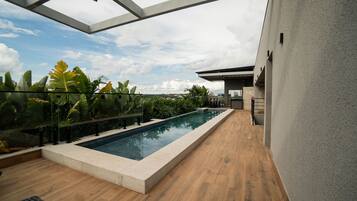 Un área de piscina en la azotea con vistas despejadas del horizonte urbano, rodeada de exuberante vegetación y arquitectura moderna.