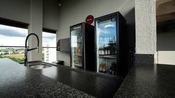 Una cocina con dos refrigeradores llenos de bebidas, un lavamanos y un ventanal con vistas a un paisaje urbano.