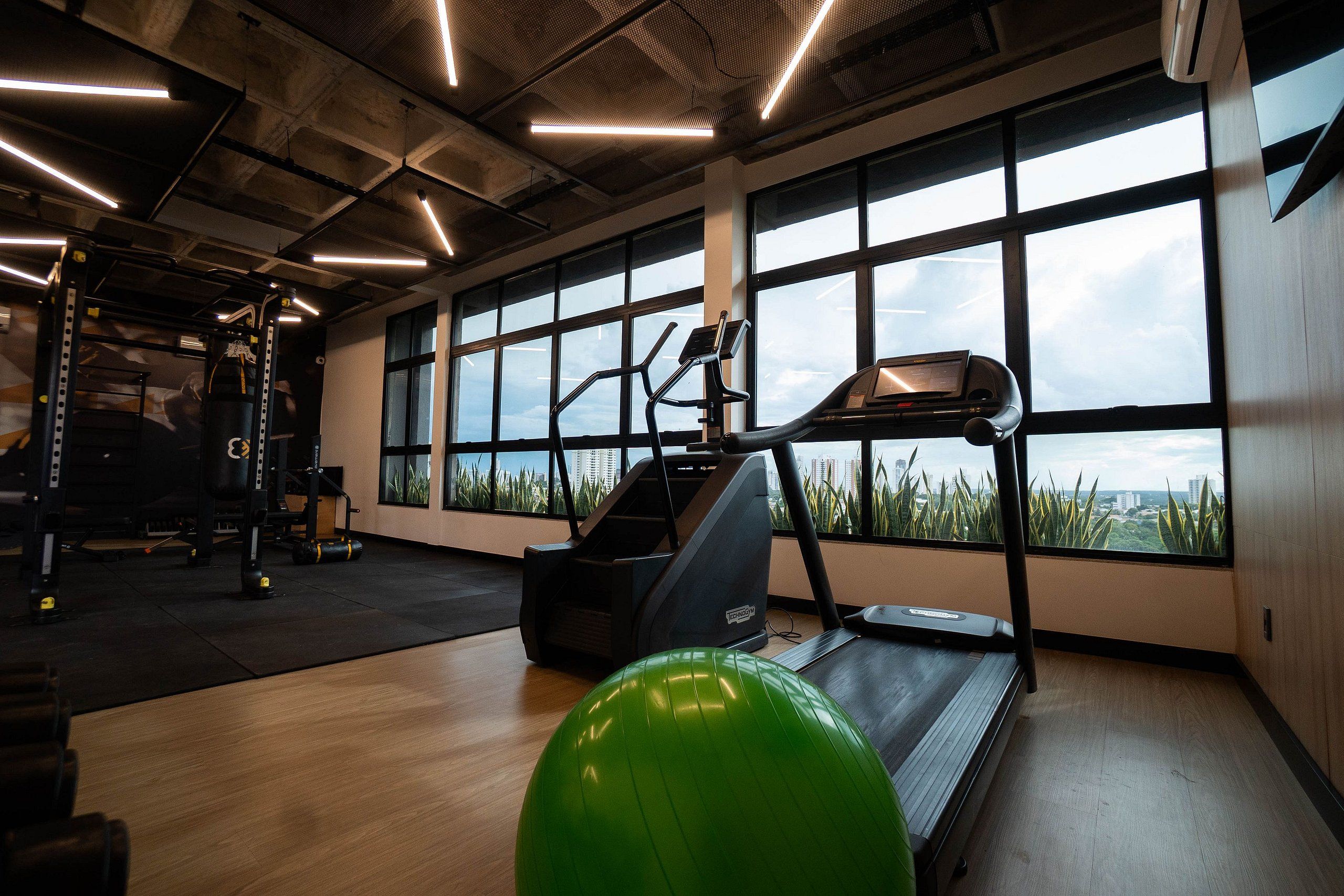 Un gimnasio con equipo de ejercicio, ventanas amplias y vistas de la ciudad.