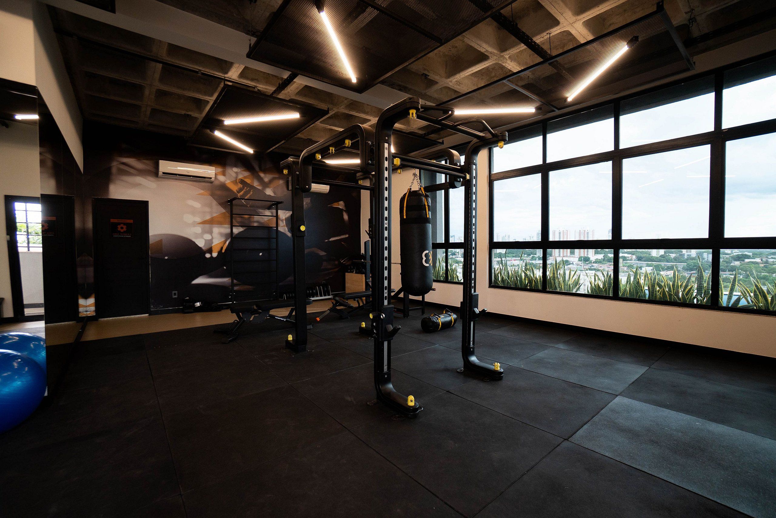 Un gimnasio con equipo de ejercicio, un saco de boxeo y vistas de un paisaje urbano a través de amplias ventanas.