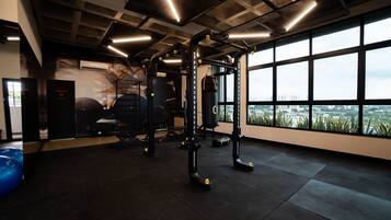 Un gimnasio con equipo de ejercicio, un saco de boxeo y vistas de un paisaje urbano a través de amplias ventanas.