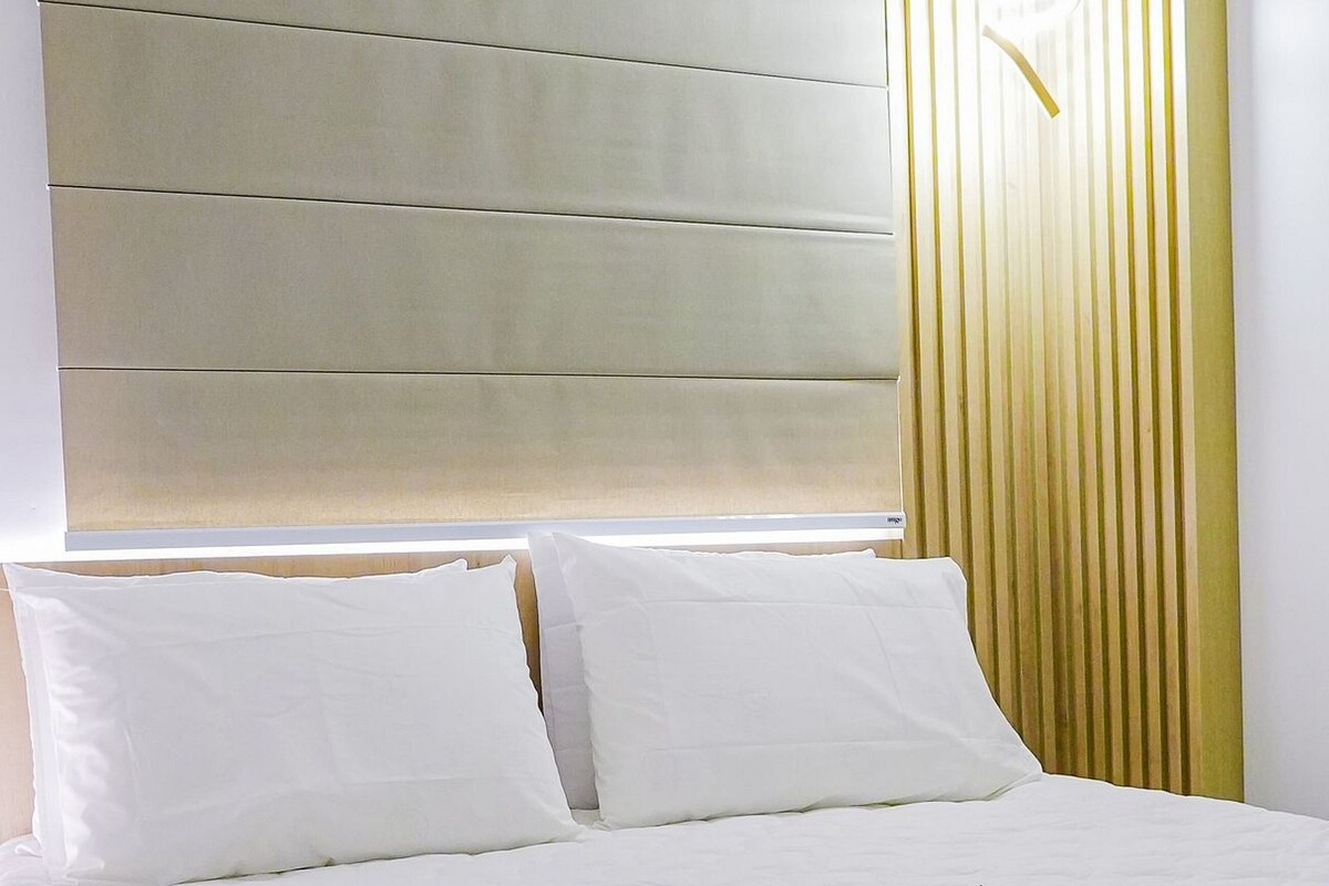 Una habitación de hotel con una cama grande, cabecera con paneles horizontales y una lámpara fijada a la pared.
