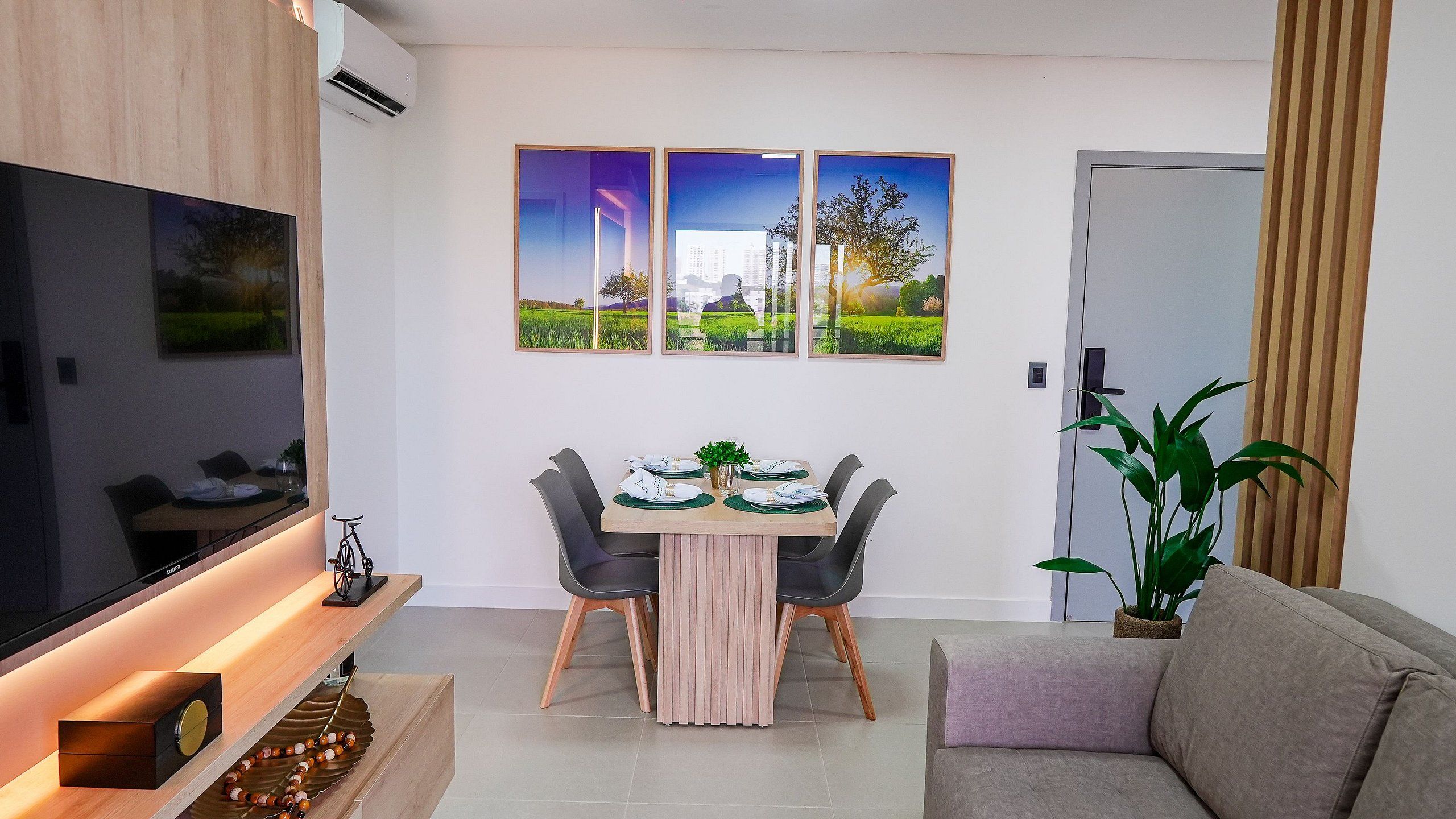 Un salon moderne avec un téléviseur à écran plat, une table à manger avec des chaises et un canapé. Trois tableaux encadrés sont accrochés au mur au-dessus de la table à manger.