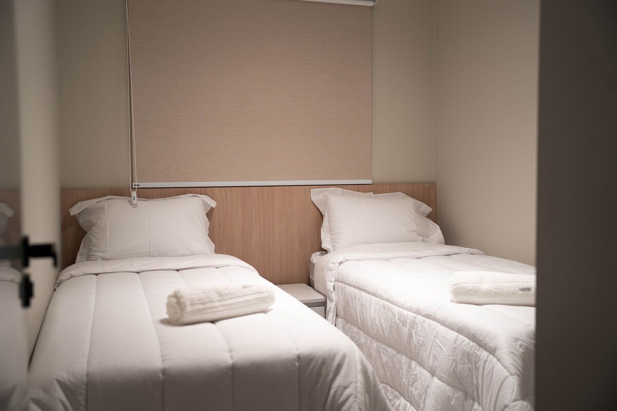 A hotel room with two single beds, each with a white duvet and a neatly folded towel.