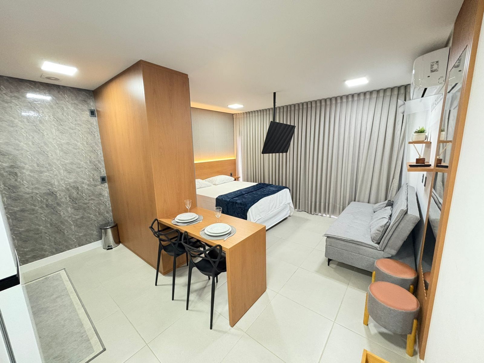 Een kleine hotelkamer met een bed, een bureau met stoelen, een bank en een televisie.