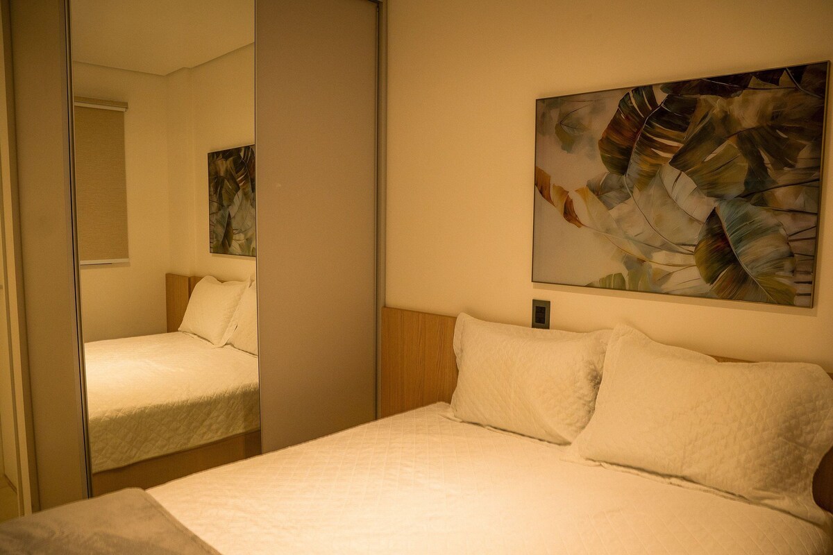 A hotel room with a bed, a mirror, and a painting on the wall.