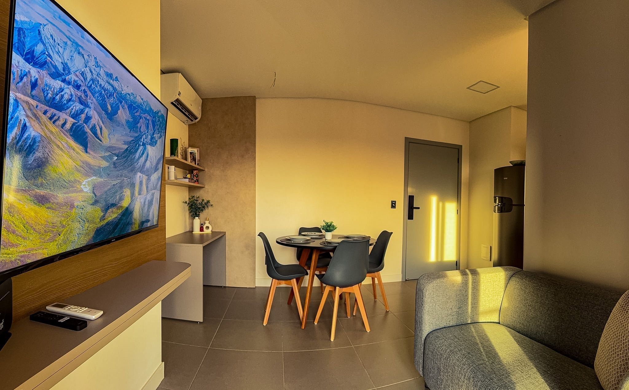A modern living room with a flat-screen TV, a dining area with a table and chairs, and a sofa.