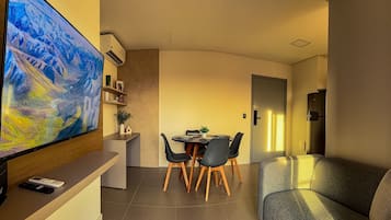 A modern living room with a flat-screen TV, a dining area with a table and chairs, and a sofa.