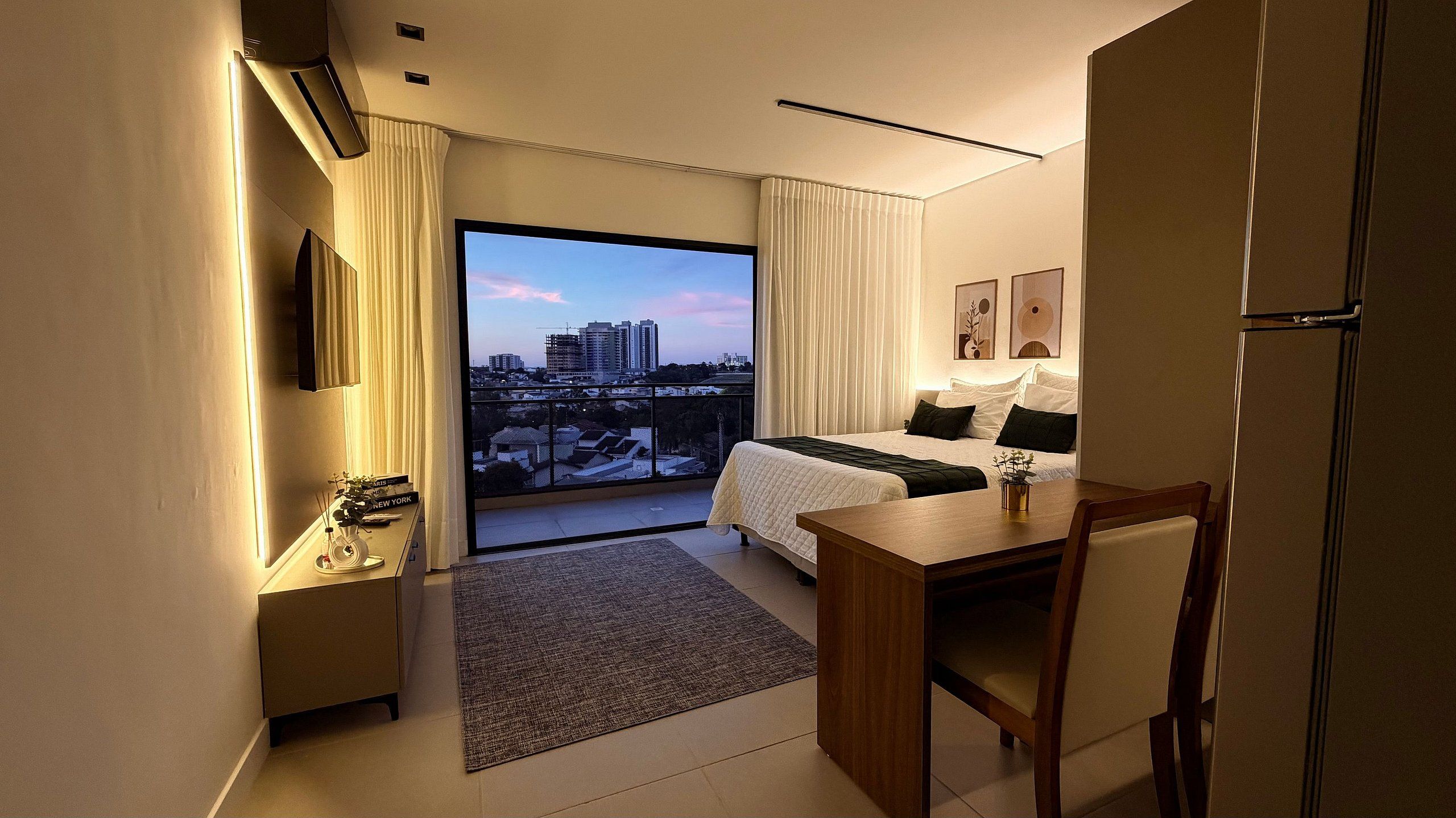 A hotel room with a bed, a desk, a chair, a small table, a TV, and a view of the cityscape.