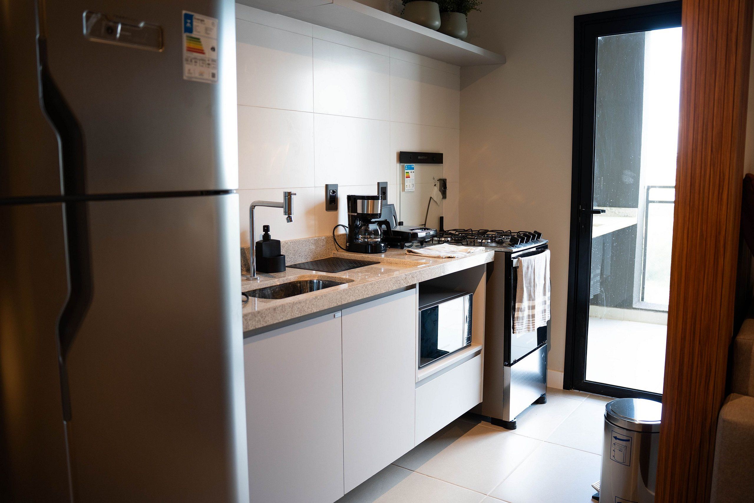 Una cocina moderna con refrigerador, pileta, estufa y cafetera.