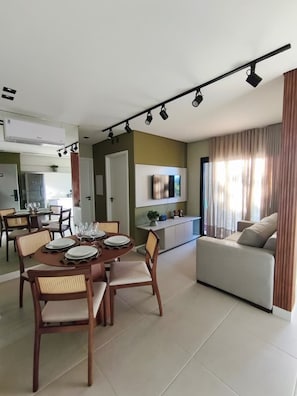 A modern living room with a sofa, dining table set for four, and a kitchen in the background. - Moov Smart Home (Cuiabá)