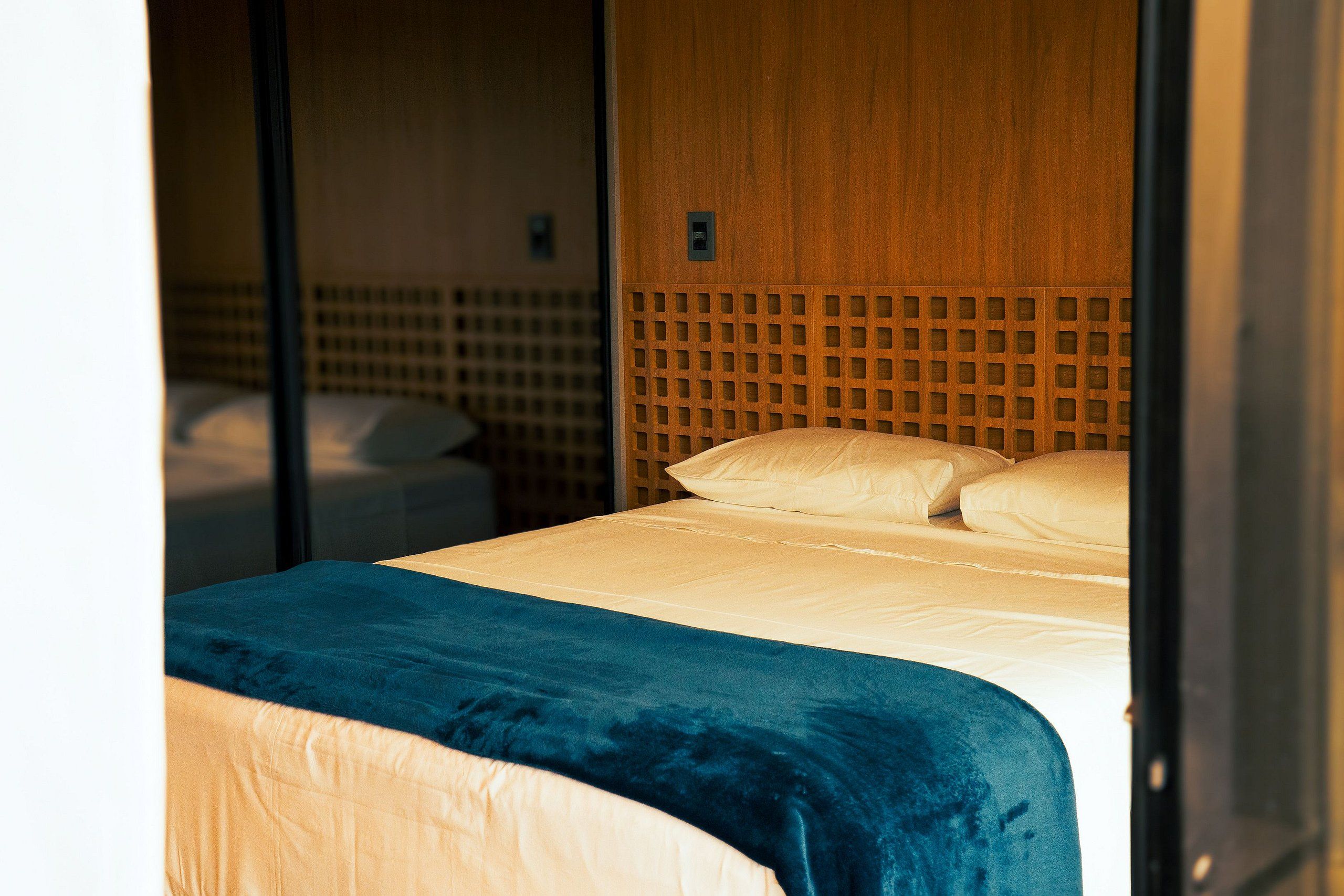 Een hotelkamer met een bed, een houten hoofdeinde en een blauwe deken.