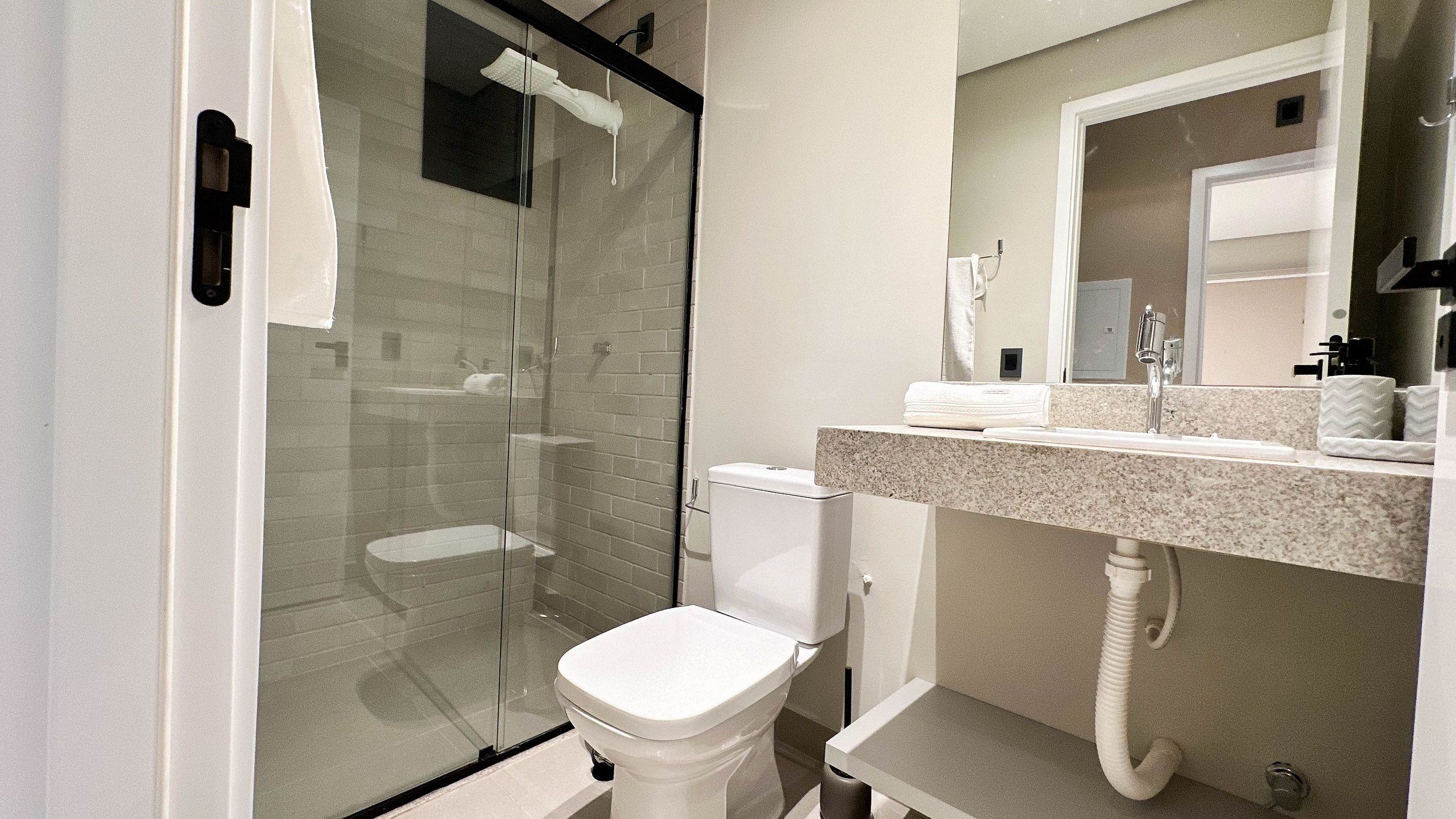 A modern bathroom with a glass shower enclosure, a white toilet, and a granite countertop with a mirror above.
