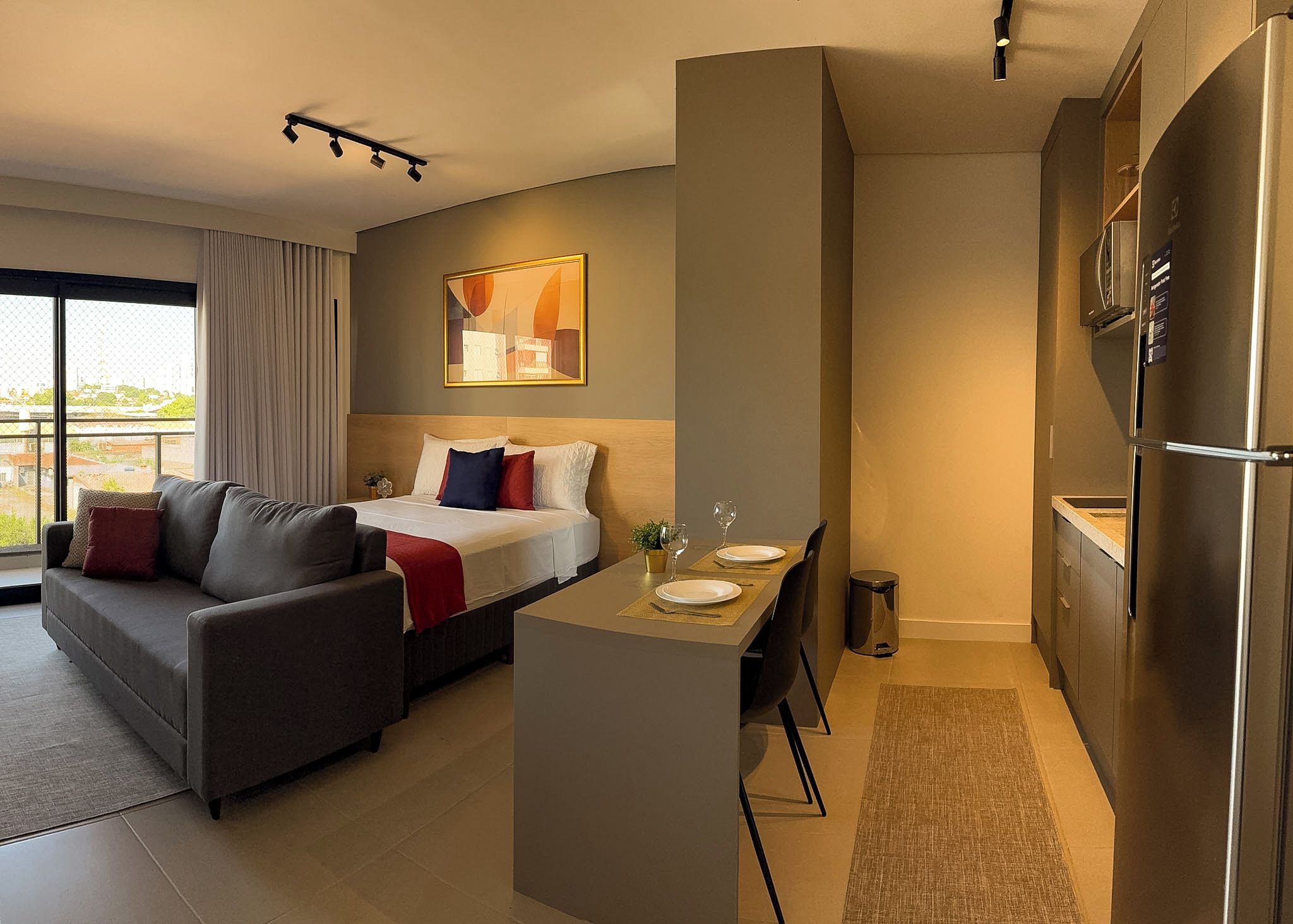 A compact living space with a bed, sofa, dining area, and kitchenette.