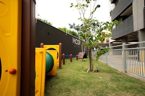 A playground with yellow play structures and a small tree in a grassy area. - Moov Smart Home (Cuiabá)