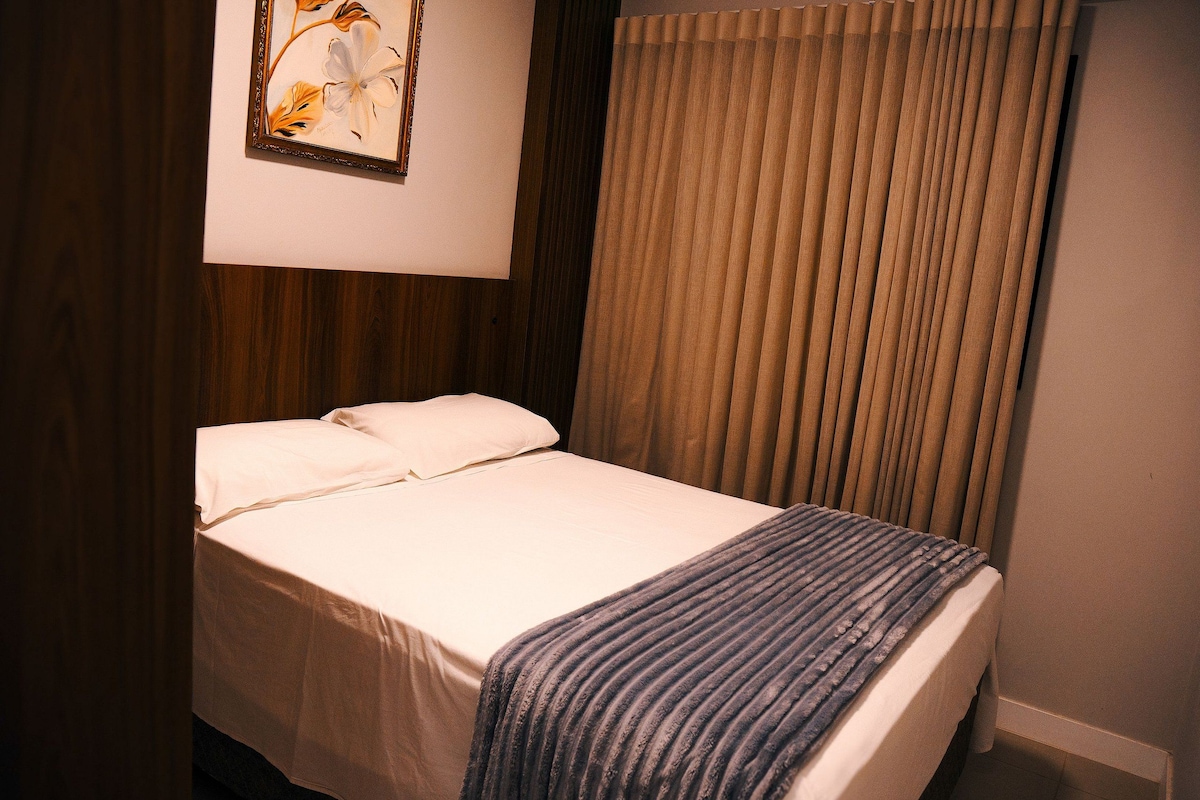 A hotel room with a bed, a pillow, a blanket, a painting, and a curtain.