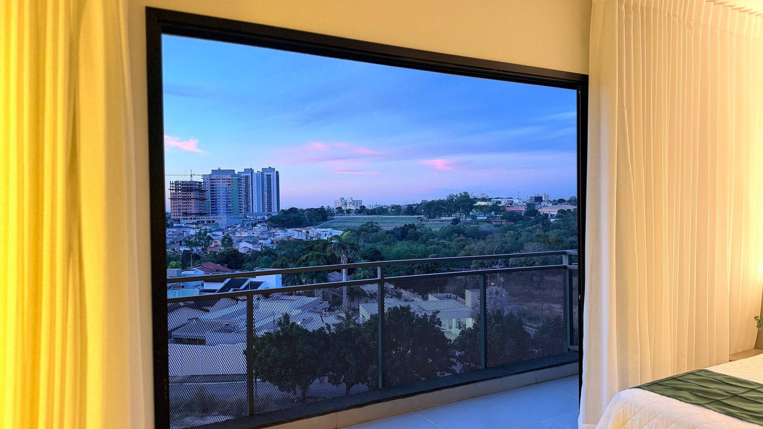 A room with a large window overlooking a cityscape at dusk.