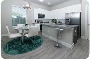 A modern kitchen with white cabinets, stainless steel appliances, a bar area, and a dining set. - Nice 3-bedroom house with AC in friendly Houston neighborhood (Houston)