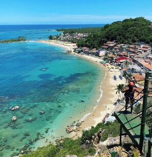 A coastal town with a beach, clear waters, and a person on a zip line.