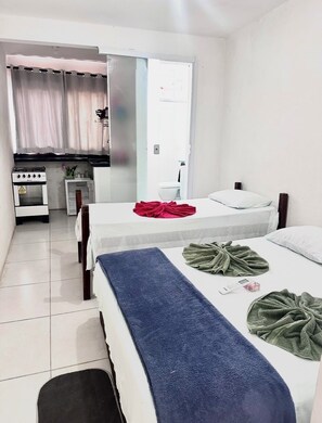 A hotel room with a bed, a small kitchenette, a bathroom, and a view of the street.
