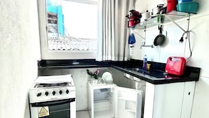 Una cocina compacta con estufa a gas, un refrigerador pequeño y una ventana con cortinas.