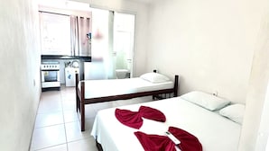 Una habitación pequeña y limpia con una cama, una mesita de noche, una ventana y una kitchenette.