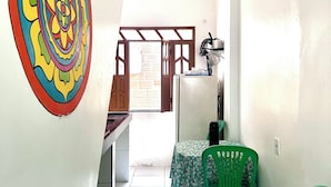 Una habitación con una decoración de pared colorida, una silla verde, una mesa con mantel floral y una zona de cocina con refrigerador y lavamanos.