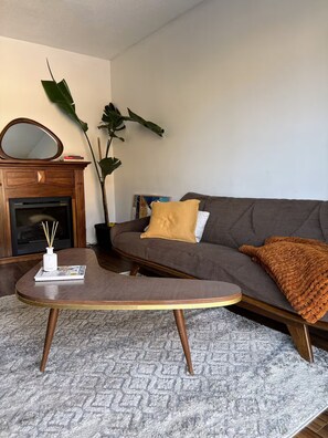 Una sala de estar con sofá, mesa de centro, chimenea y una planta grande.