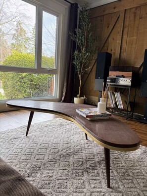Ein Zimmer mit einem gebogenen Holztisch, einer Topfpflanze, einer kleinen weißen Vase und einem Bücherregal mit Büchern und einem Plattenspieler.