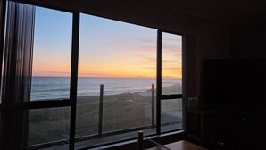 A room with a large window overlooking a coastal view, a television, and a small table. - Ben Avon Views - Cape Palliser/Ngawi
Stunning ocean veiws, Fireplace & BBQ (Cape Palliser)