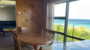 A dining area with a wooden table and chairs, a view of the ocean, and a wooden wall. - Ben Avon Views - Cape Palliser/Ngawi
Stunning ocean veiws, Fireplace & BBQ (Cape Palliser)