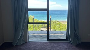 A room with a large sliding glass door leading to a balcony with a view of the ocean. - Ben Avon Views - Cape Palliser/Ngawi
Stunning ocean veiws, Fireplace & BBQ (Cape Palliser)