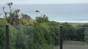 A coastal road leading to a beach with lush greenery and a view of the ocean. - Ben Avon Views - Cape Palliser/Ngawi
Stunning ocean veiws, Fireplace & BBQ (Cape Palliser)
