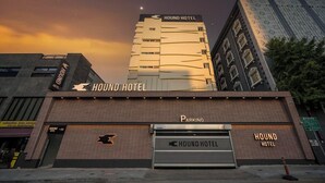 A HOUND HOTEL building with a prominent sign, a parking garage entrance, and a large building in the background.