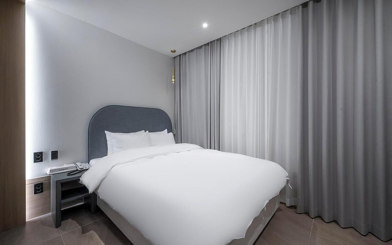 A modern hotel room with a large bed, a bedside table with a phone, and a curtain.