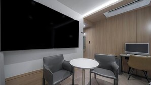 A modern room with a large flat-screen TV, two grey sofas, a small round table, and a wooden panel wall.