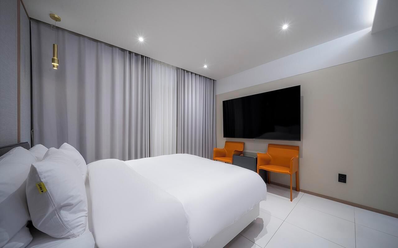 A modern hotel room with a large bed, a flat-screen TV, and two orange chairs.