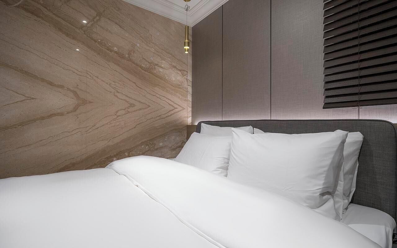 A modern bedroom with a marble wall, a bed with white linens, and a headboard.