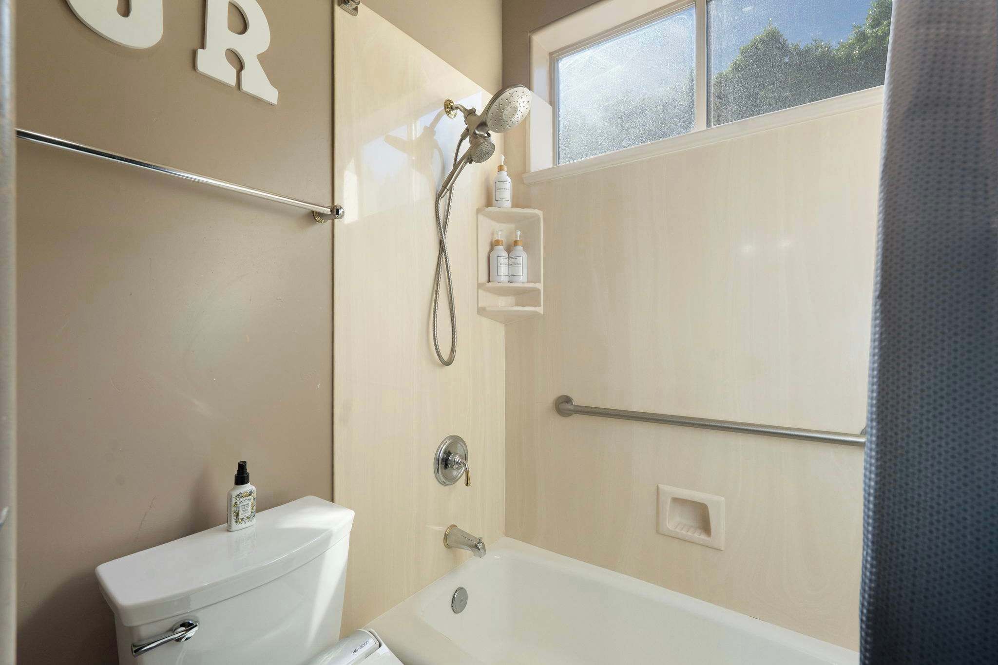 Un baño con inodoro, bañera, ducha con cabezal de mano y estante con artículos de aseo.