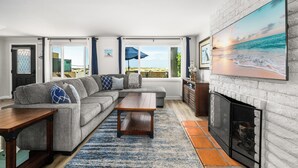 A living room with a sectional sofa, a coffee table, a fireplace, and a large beach painting. - Oceanfront Stay Near Newport Boardwalk (Newport Beach)