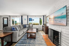 Ein Wohnzimmer mit einer Eckcouch, einem Couchtisch, einem Kamin und einem großen Strandbild.