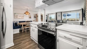 A modern kitchen with white cabinetry, a built-in oven, and a dining area with a wooden table and blue upholstered seating. - Oceanfront Stay Near Newport Boardwalk (Newport Beach)