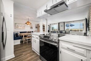 Eine moderne Küche mit weißen Schränken, einem eingebauten Ofen und einem Essbereich mit Holztisch und blau bezogenen Sitzmöglichkeiten.